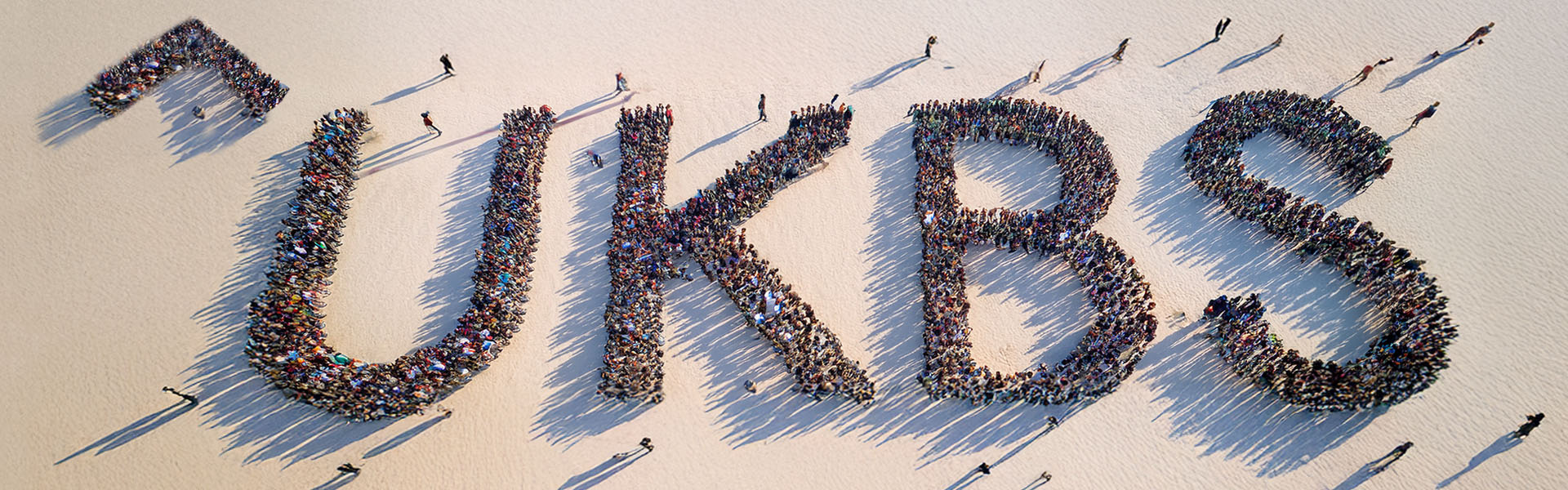 Eine Luftaufnahme vieler Menschen am Strand, die sich zum UKBS-Logo formiert haben.
